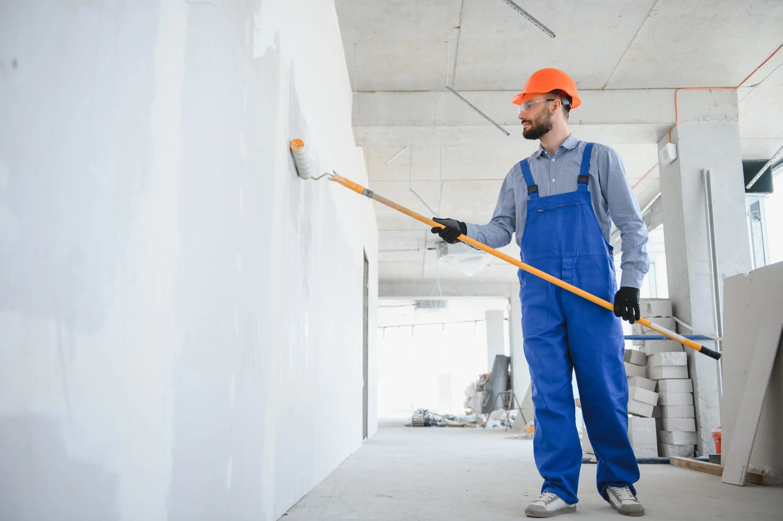 Professional commercial painter in blue uniform using roller on white interior wall by Bos-Flo Coatings