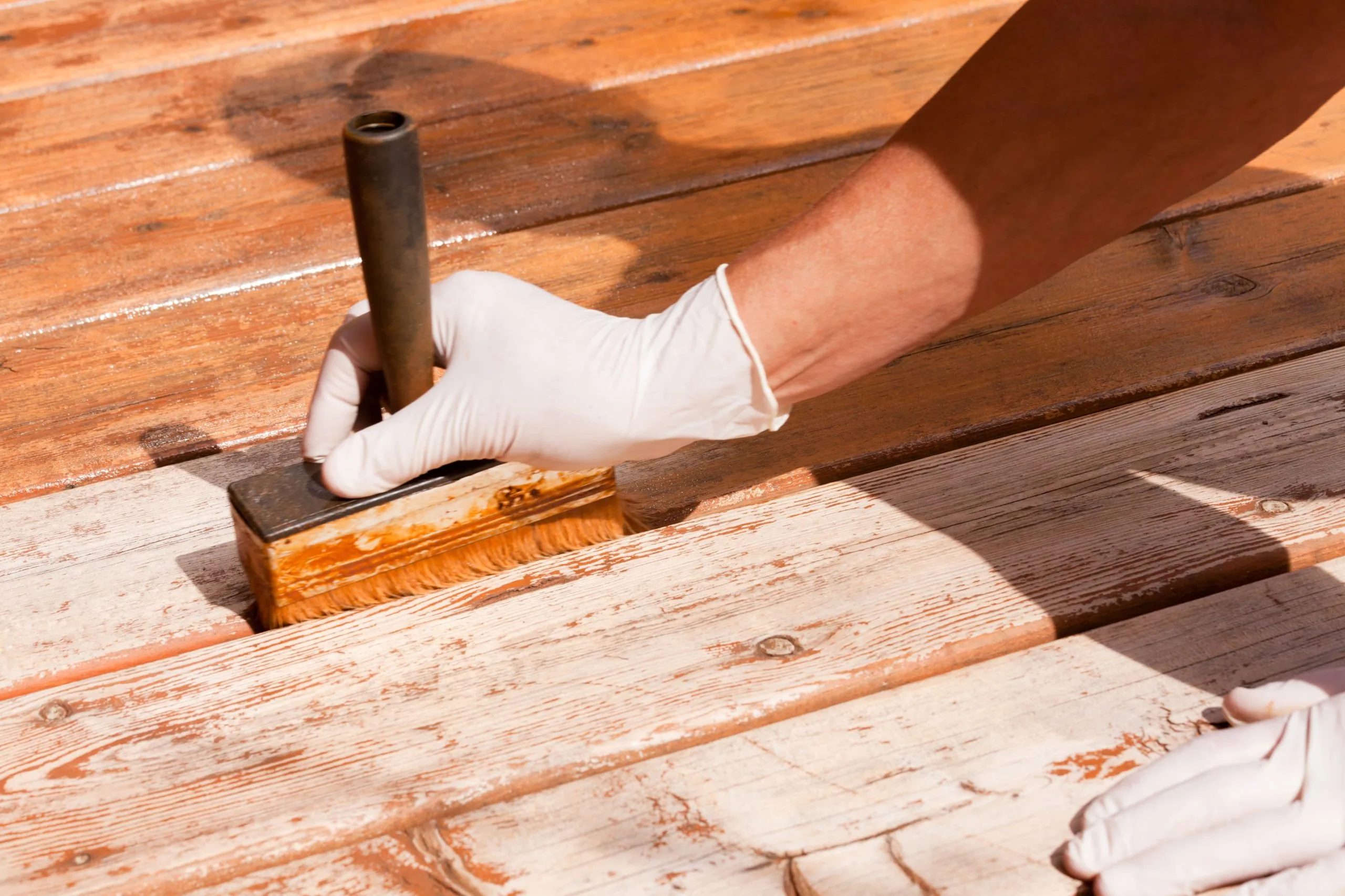 Close-up of professional deck staining with brush application on weathered wooden planks by Bos-Flo Coatings