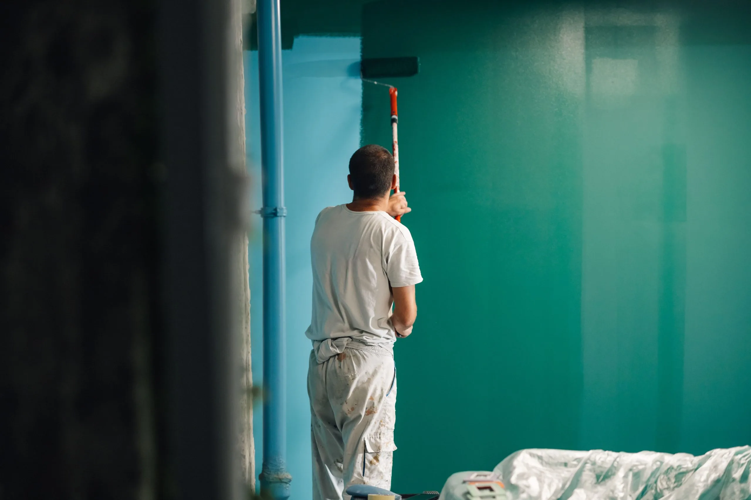 Professional painter applying green paint with roller on interior wall — Bos-Flo Coatings