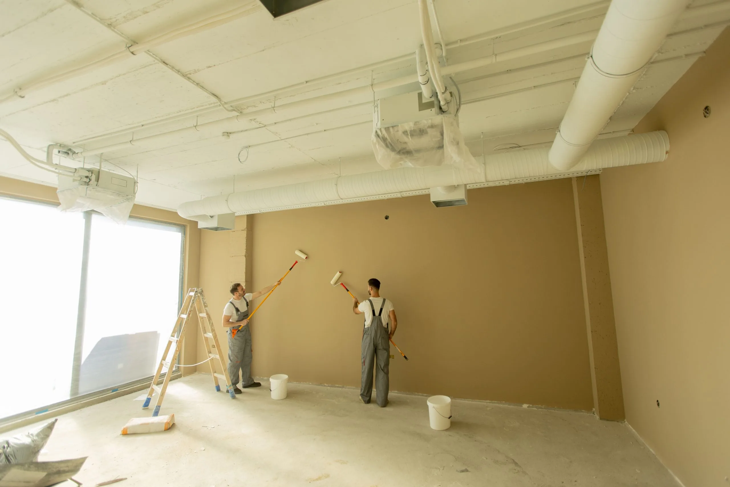 Two professional painters in overalls rolling brown paint on commercial interior wall by Bos-Flo Coatings
