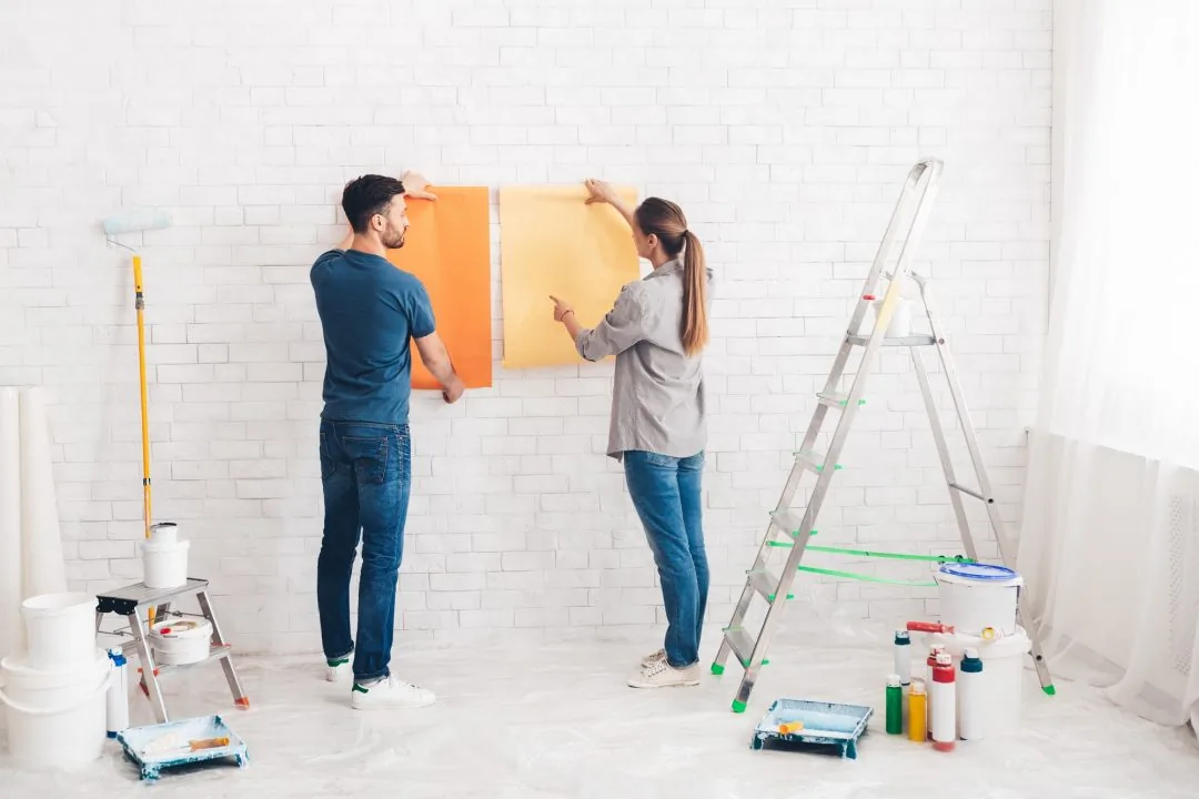 Couple comparing paint color samples on a white brick wall before painting