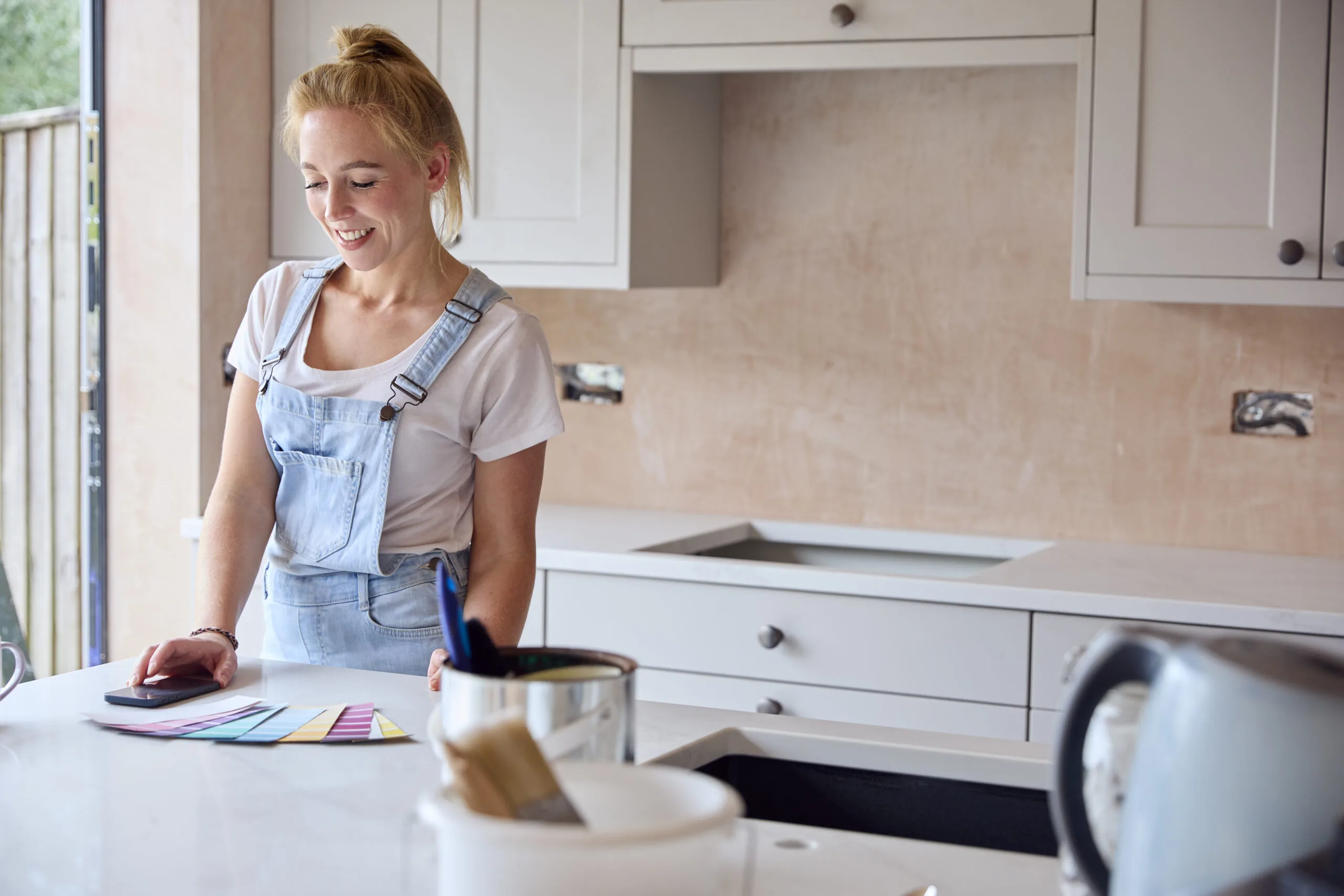 Woman in denim overalls choosing paint colors for kitchen cabinets during renovation